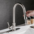 Stainless steel kitchen faucet with hand holding a spray head over a sink.