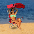 Woman in a green bikini sitting on a red beach chair with an umbrella, ocean in the background